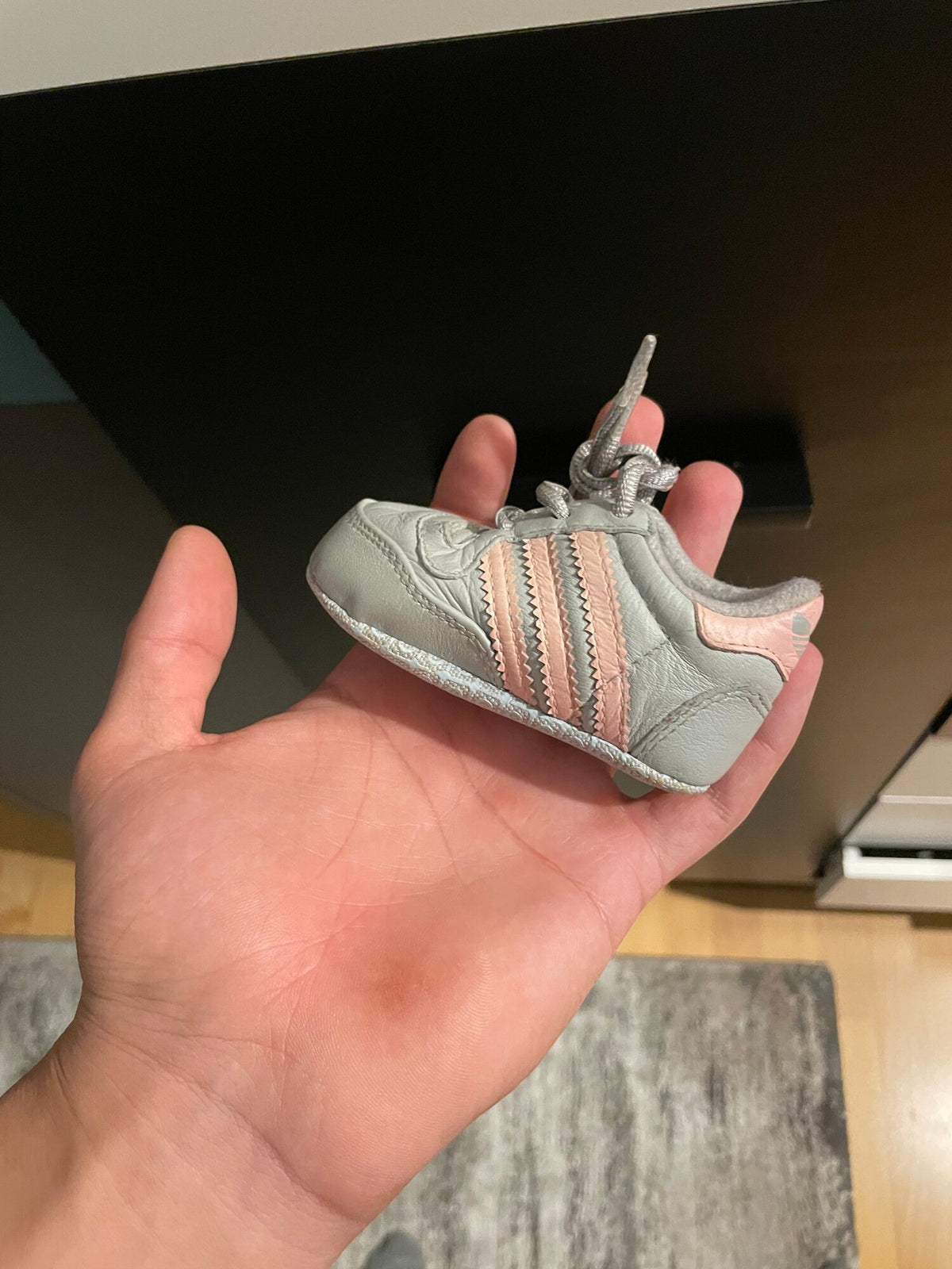 A tiny grey-and-pink baby sneaker in the palm of a hand