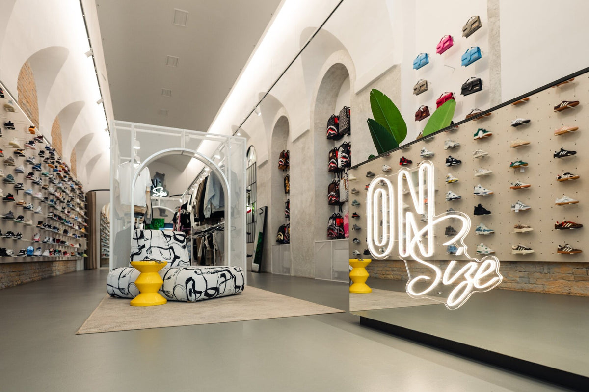 OnSize neon sign on the mirrored counter, with bags and sneakers behind it