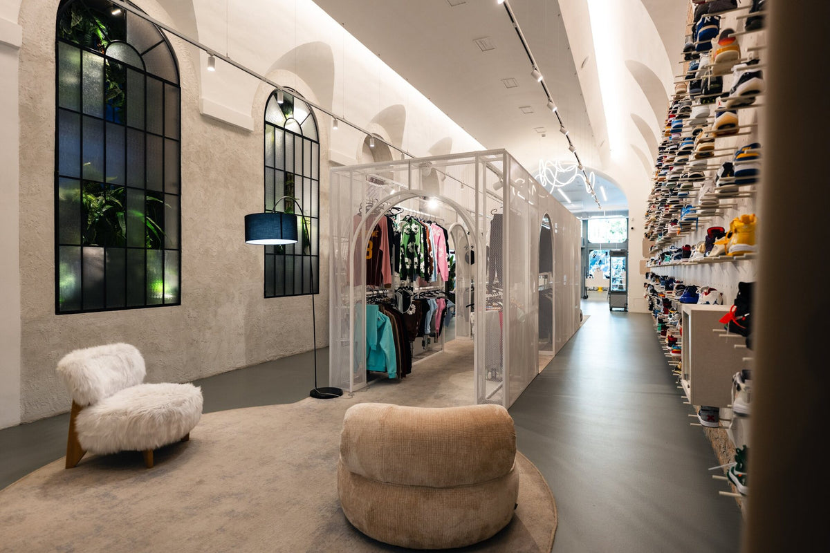 Lounge corner with a fur armchair and a pouf at the back of the store, next to a sneaker wall
